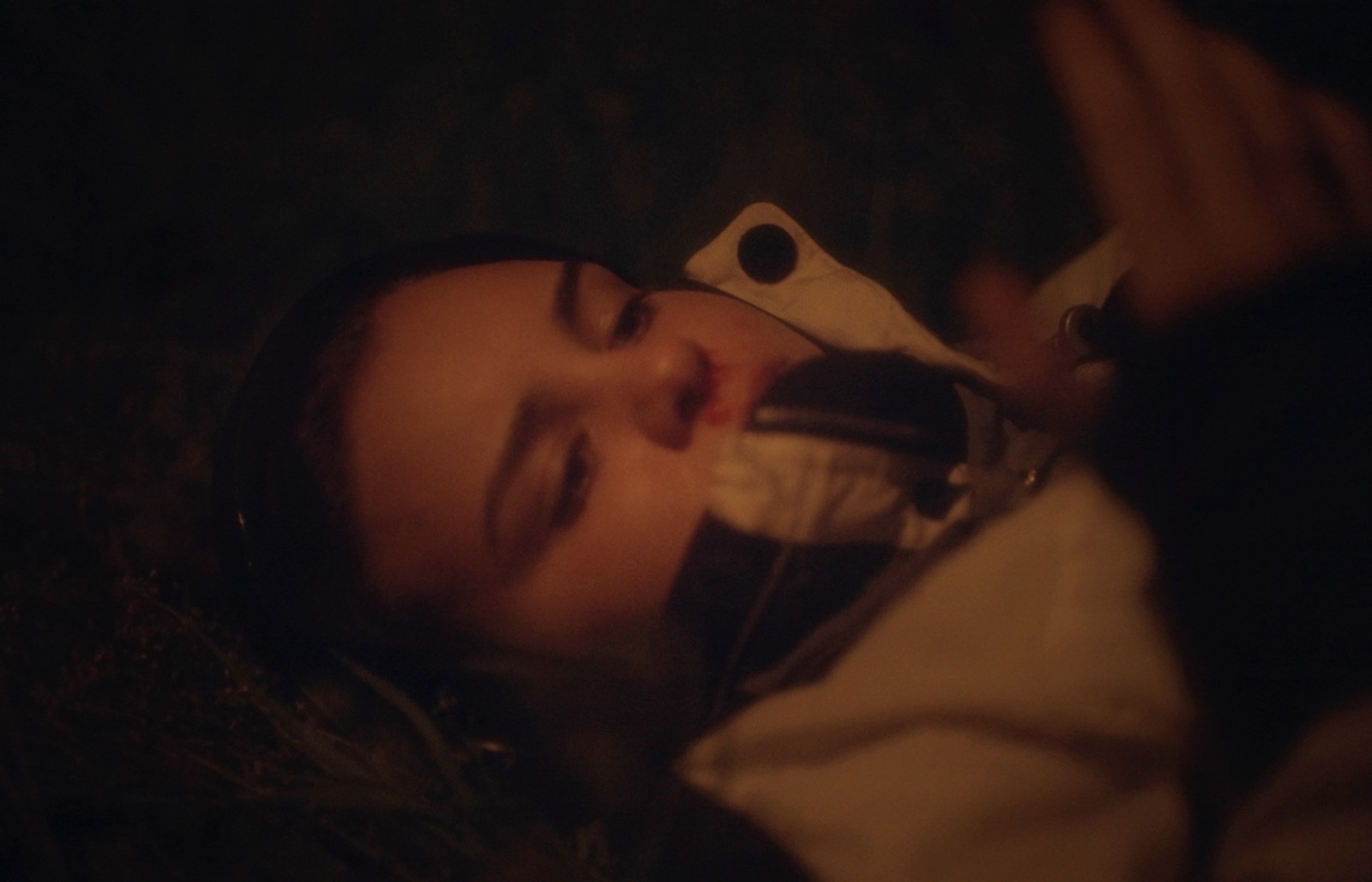 A film still with a close-up on a young girl’s face with a nosebleed, lit only by a faint ember.