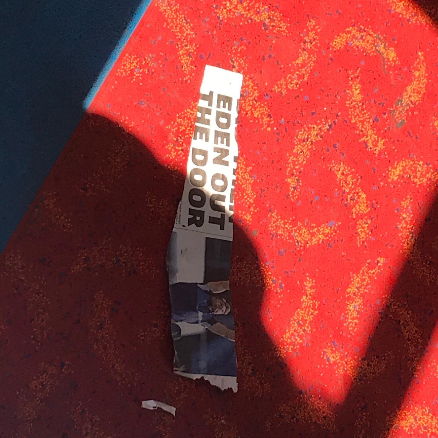 On the floor of a London bus, a ripped bit of a page from a newspaper where one can read: EDEN OUT THE DOOR.